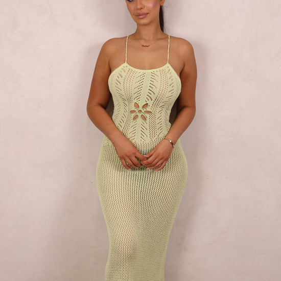 A model wearing a pale green crochet knit maxi dress with a floral waist cut-out and open criss-cross back.