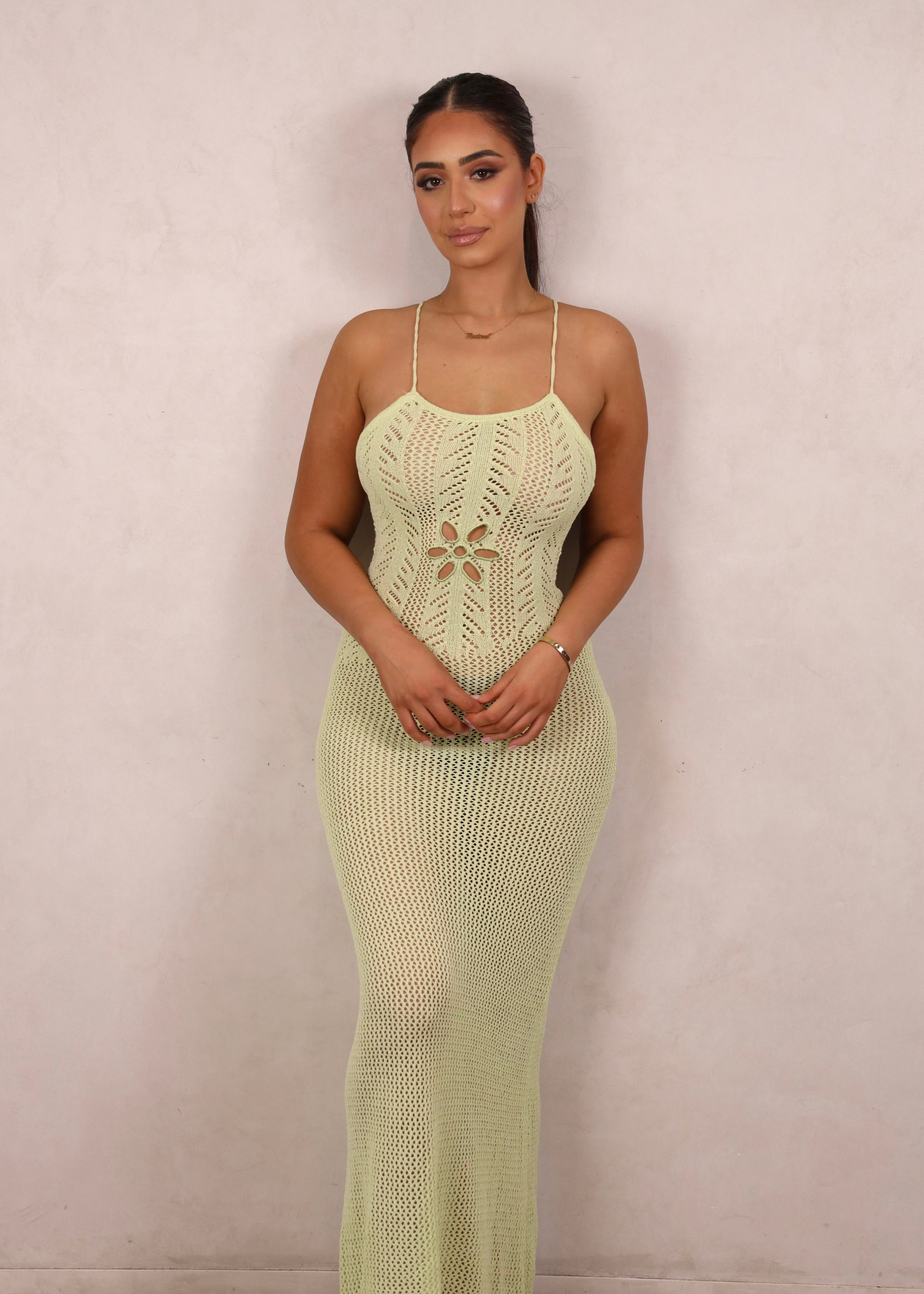 A model wearing a pale green crochet knit maxi dress with a floral waist cut-out and open criss-cross back.