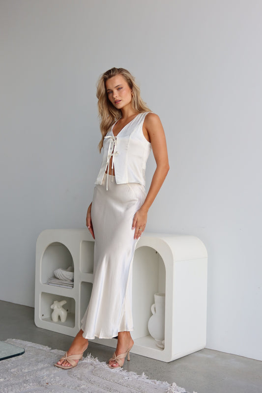 A woman wearing a white satin vest with a tie front and V-neck, sleeveless vest-style design.