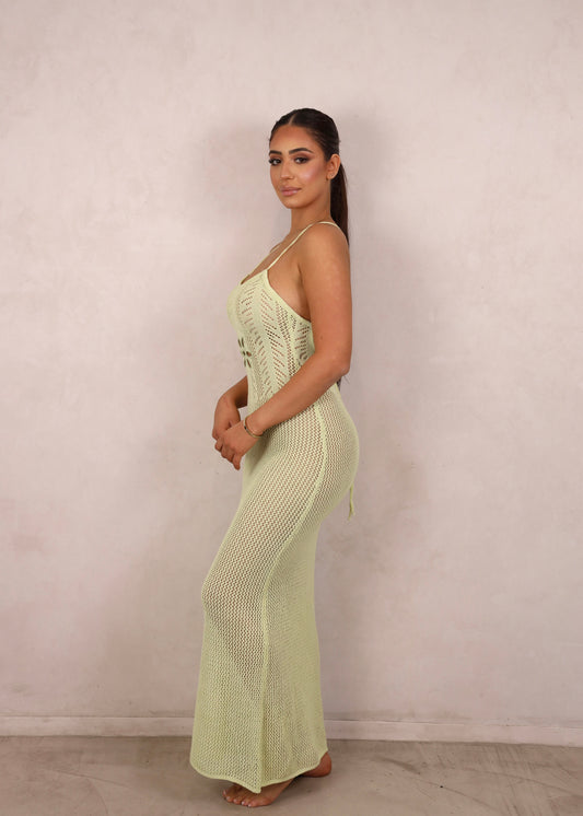 A model wearing a pale green crochet knit maxi dress with a floral waist cut-out and open criss-cross back.