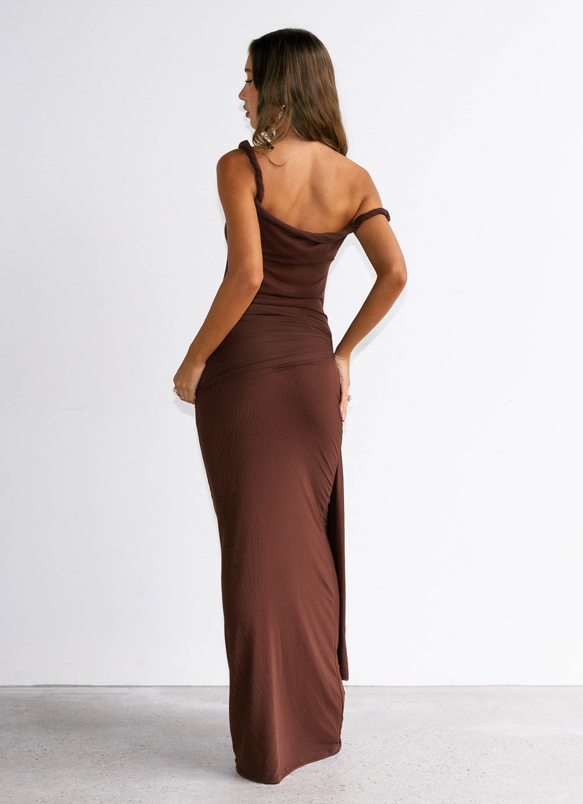 Woman wearing a brown one-shoulder dress with a slit on a white background