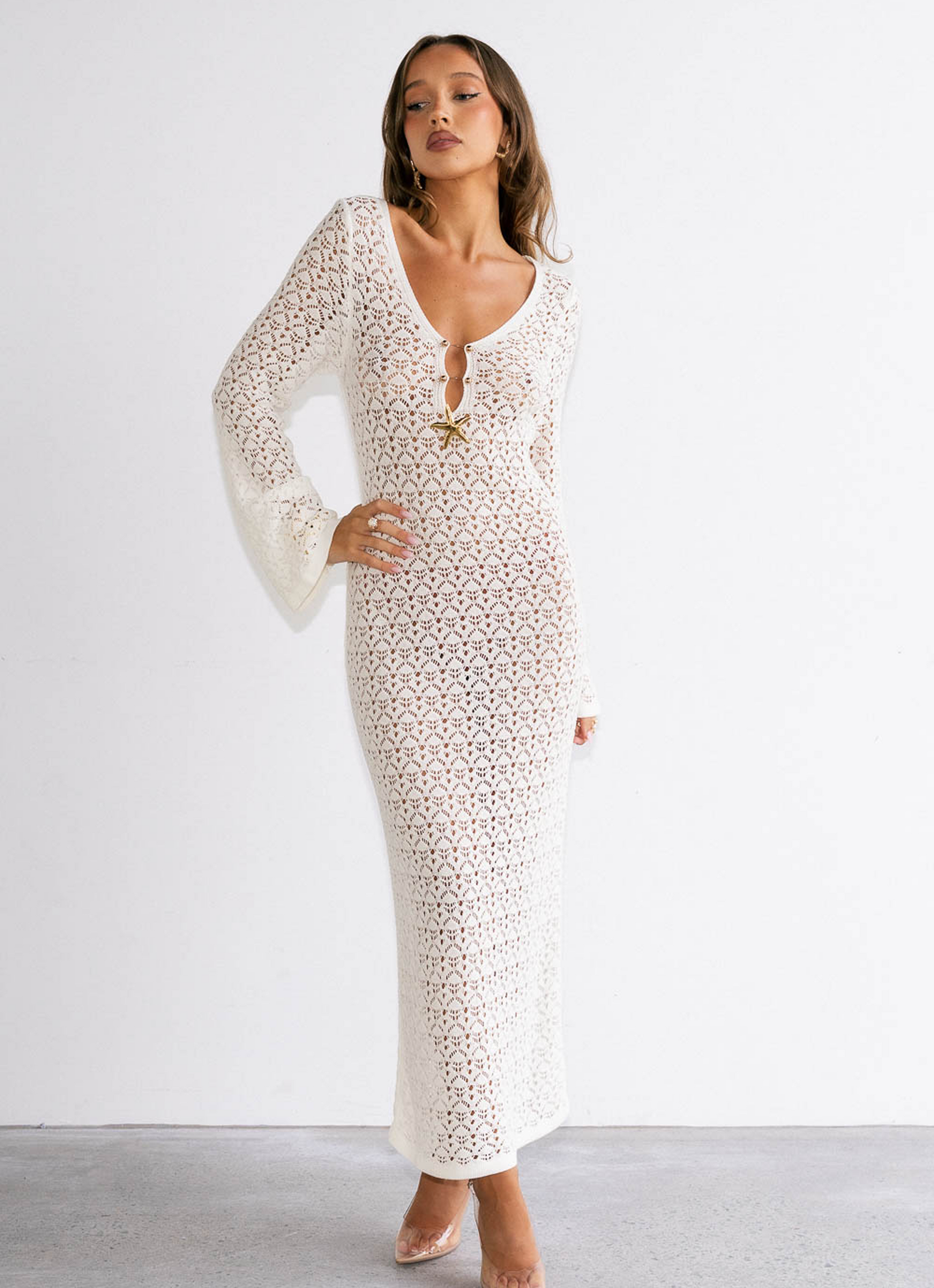 Woman wearing a white lace dress with sheer sleeves against a plain background