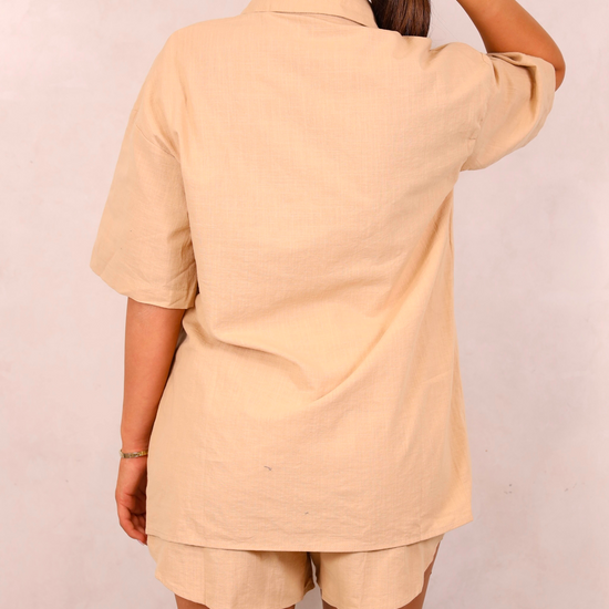 Person wearing a beige outfit with shorts on a plain background