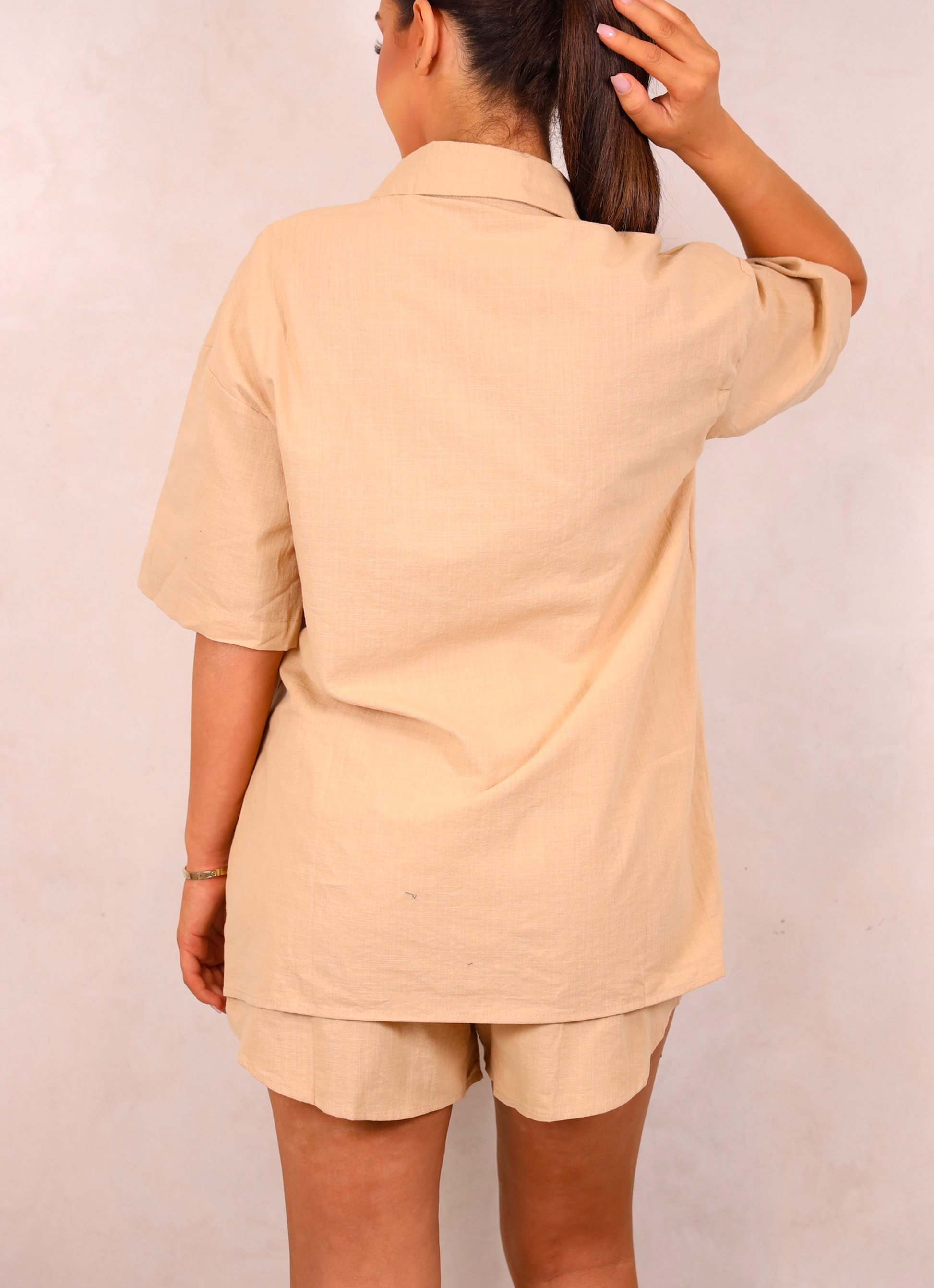 Person wearing a beige outfit with shorts on a plain background