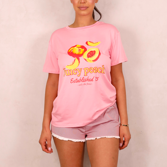 Woman wearing a pink t-shirt with 'juicy peach' design on a plain background