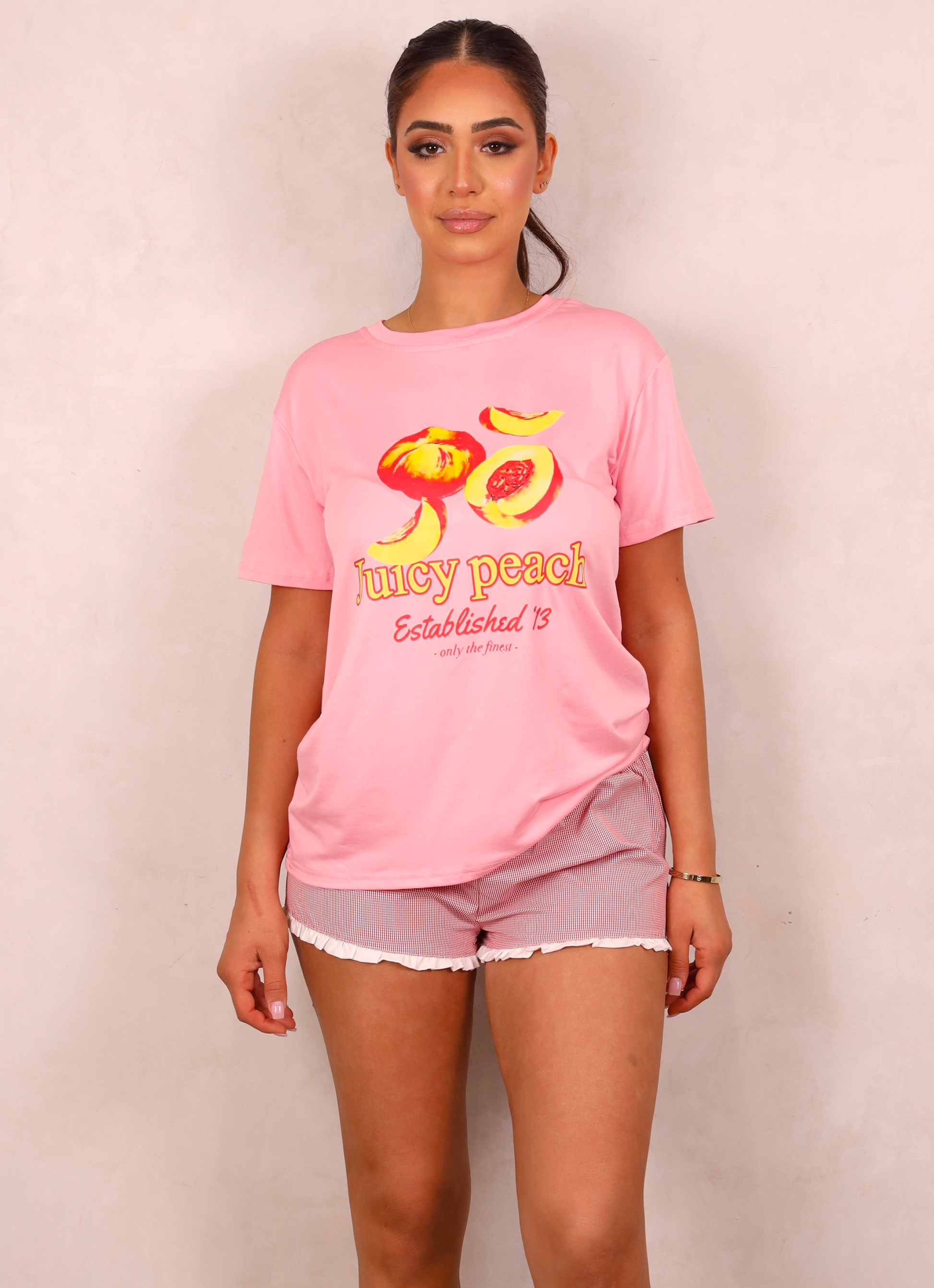 Woman wearing a pink t-shirt with 'juicy peach' design on a plain background