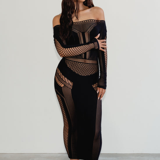 Woman wearing a black off-shoulder dress with mesh panels on a white background