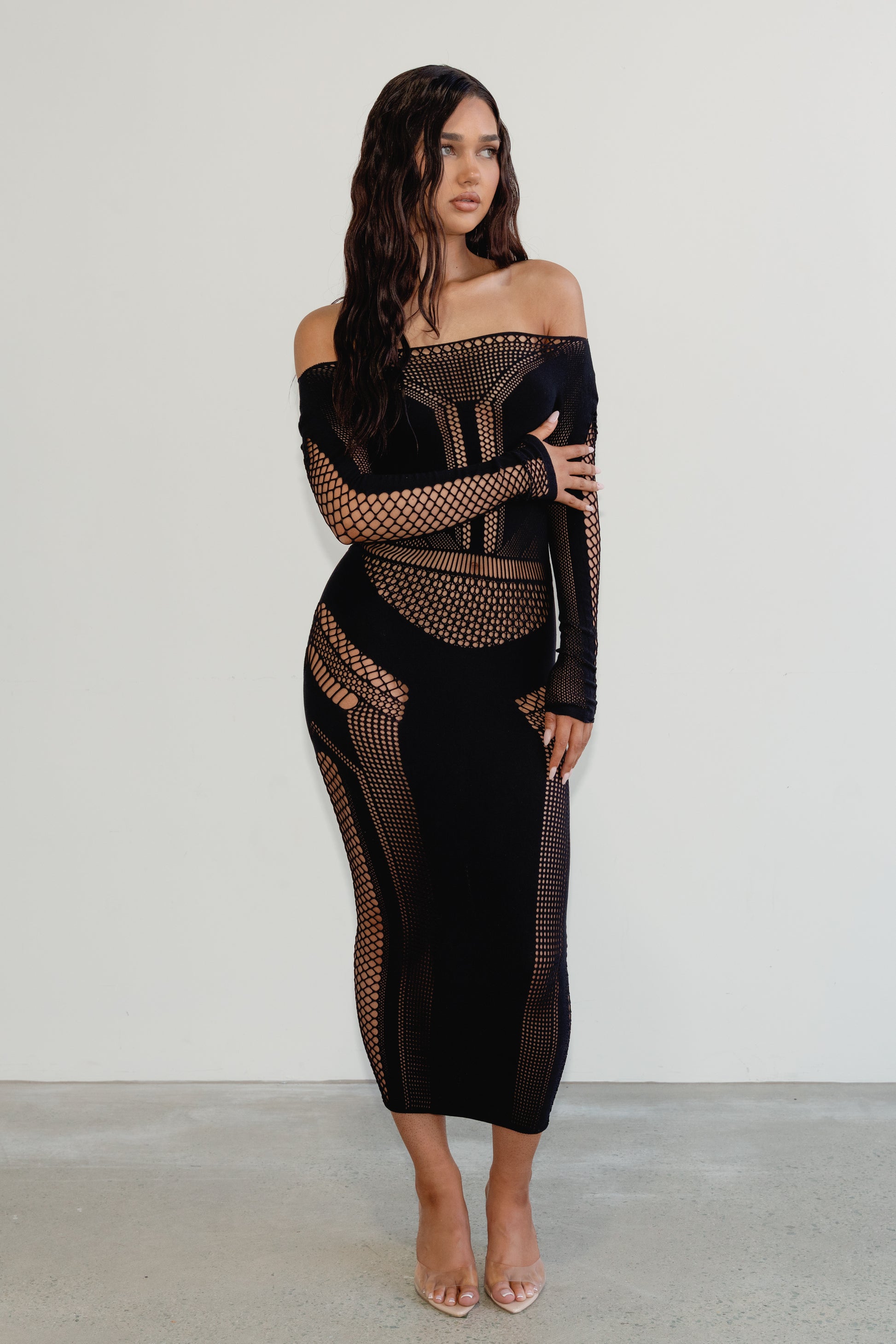Woman wearing a black off-shoulder dress with mesh panels on a white background