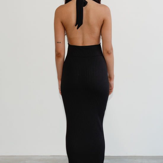 Woman wearing a black halter neck dress with a plain background