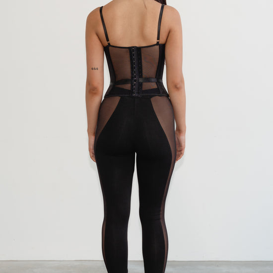 Person wearing a black mesh jumpsuit on a plain background