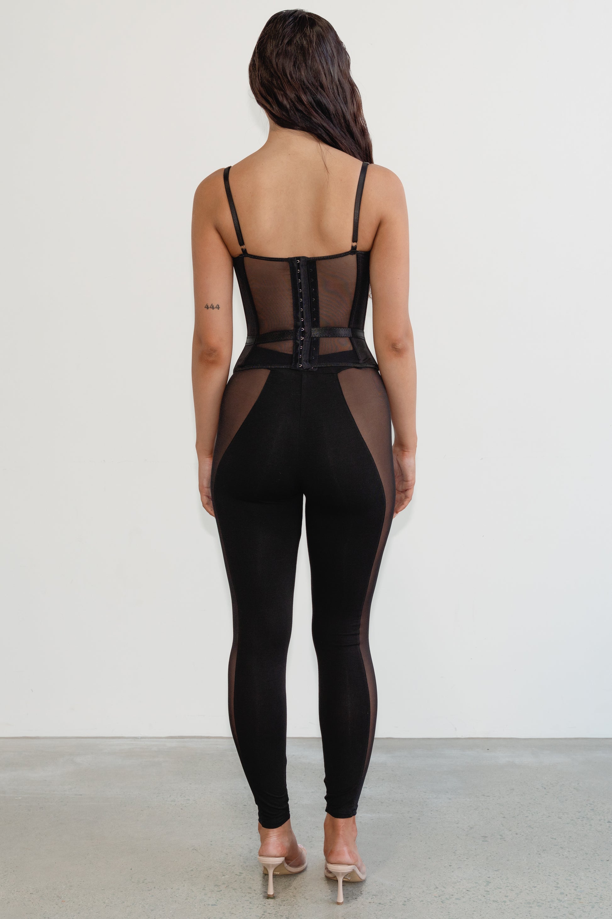 Person wearing a black mesh jumpsuit on a plain background
