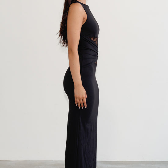 Woman wearing a black sleeveless top and high-waisted pants against a white background