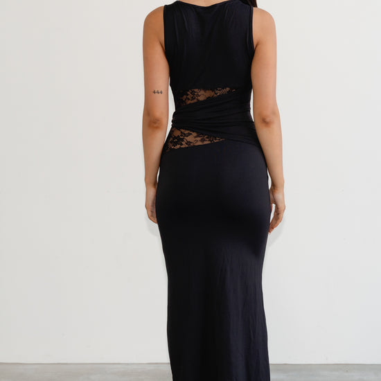 Woman wearing a black sleeveless dress with lace detailing on a plain background