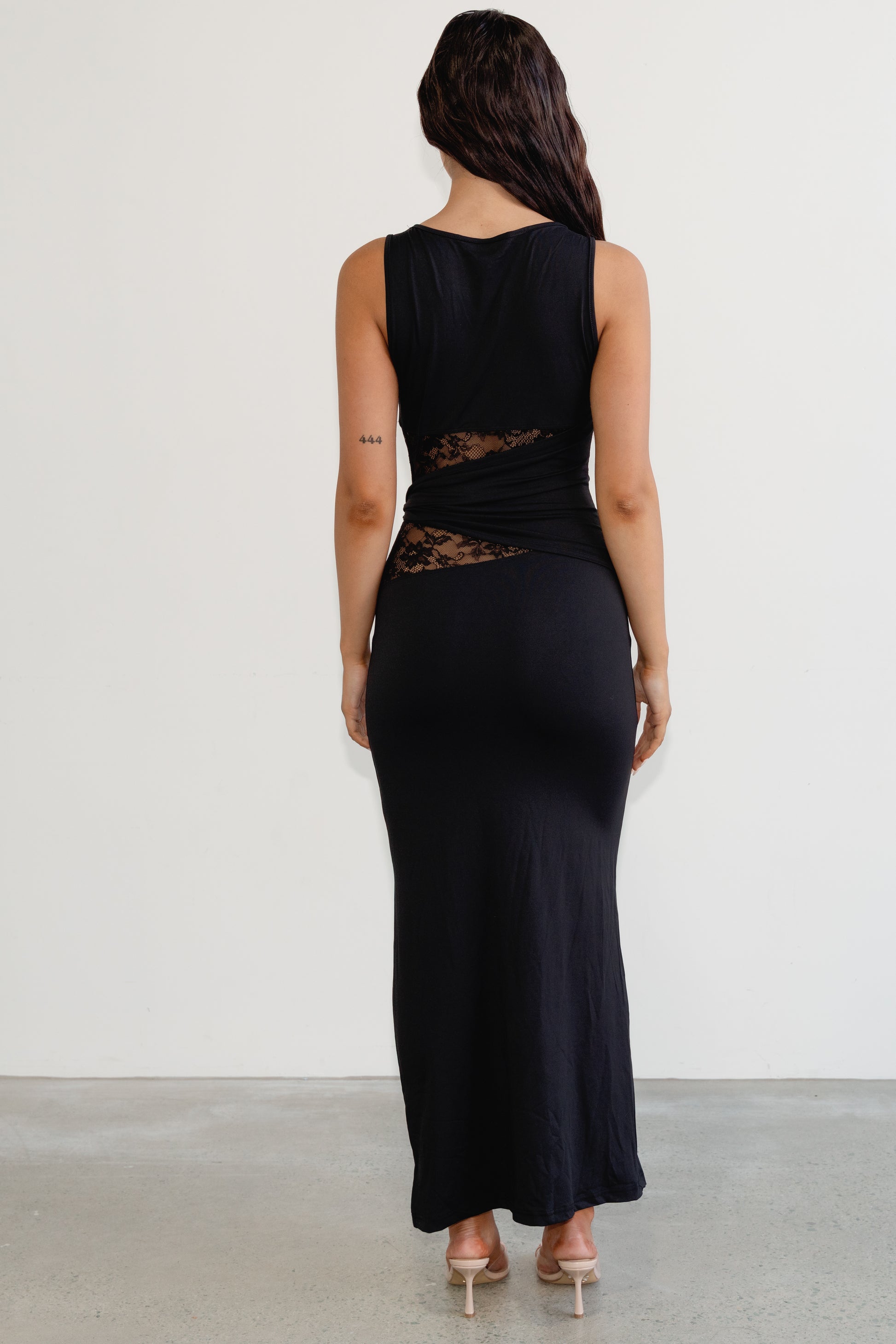 Woman wearing a black sleeveless dress with lace detailing on a plain background