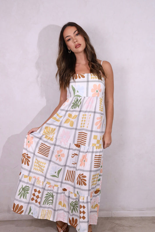A model wearing a sleeveless, tiered, patchwork floral print maxi dress with thin straps.