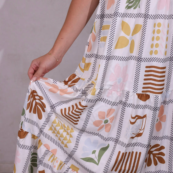 A model wearing a sleeveless, tiered, patchwork floral print maxi dress with thin straps.