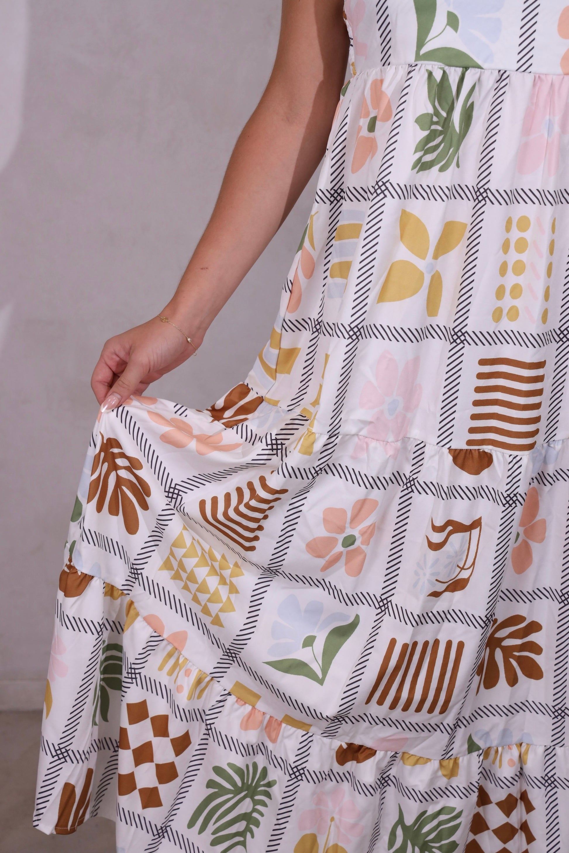 A model wearing a sleeveless, tiered, patchwork floral print maxi dress with thin straps.