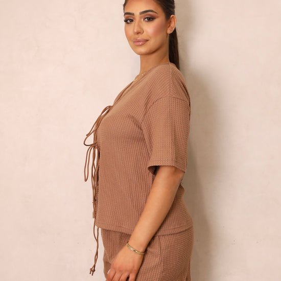 A woman wearing a brown tie-front crop top and matching shorts with a drawstring waist.
