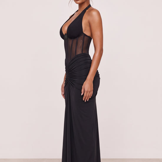 Amaya Sheer Corset Halter Maxi Dress in black, side view showing the sheer bodice, fitted waist and floor-length dress.